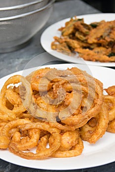 Onion ring in white dish with fried various vegetables on table.