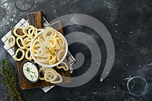 Onion rings. Fast food. Crispy onion chips in ceramic black bowl with sour cream sauce and onions in wooden stand on old black