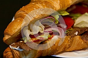 onion rings, lettuce and tomatoes in a croissant with meat and sauce