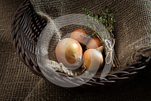 Onion and sheaf thyme in a wicker basket which stands on bu