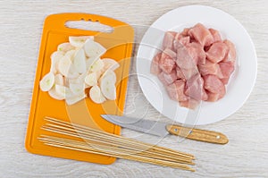 Onion and skewers on cutting board, raw chicken meat, knife