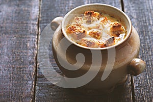 Onion soup in the ceramic pot on the wooden table horizontal