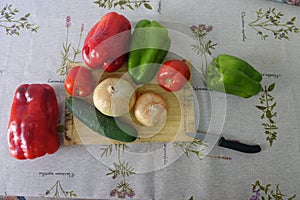 Onions, green and red Peppers and cucumber all raw and whole on a wooden board on a table with old oilcloth tablecloth