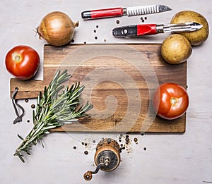 Onions, tomatoes, a bunch of rosemary, potatoes, a knife for cleaning potatoes, pepper grinder posted around cutting board