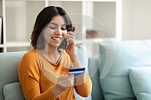 Online Banking. Smiling Arab Woman Talking On Cellphone And Holding Credit Card