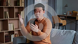 Online bet concept. Happy mature asian man looking at smartphone and enjoying win, slow motion