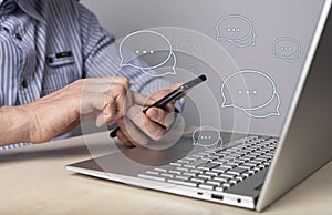 Online business communication on messengers. Man with phone in hands sitting at table with laptop and typing message to