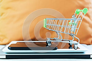 Online business and e-commerce or shopping online concept. Shopping basket on top of stack of laptop, tablet and mobile phone.
