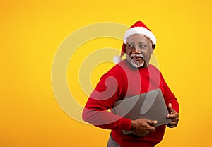 Online Christmas shopping. Senior black man with tablet computer looking aside at empty space on orange background