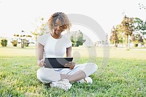 Online communication, education or work concept. Pretty African American lady with tablet computer at park