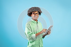 Online communiction. African american teen guy browsing web on tablet pc over blue studio background