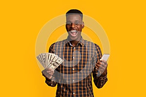 Online credit. Funny young black man holding smartphone and dollar cash