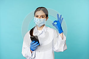 Online doctor and clinic. Young woman in medical face mask, using smartphone for client remote online appointment