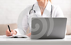 Online doctor consultation. Woman in white coat makes notes with pen and notebook