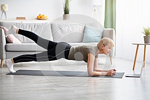 Online domestic sports concept. Mature woman exercising to video on laptop, doing elbow plank at home