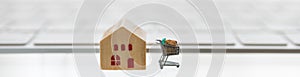 Online, E-Commerce and Technology Cover concept.  Close up of miniature shopping cart / trolley with wooden mini house toy and