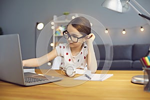 Online education of children. The girl with glasses prints a laptop lecture sitting at a table in the room