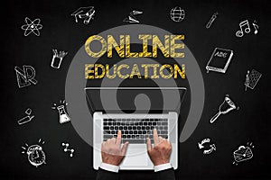 Online education concept, hands working laptop with online education concept chalk text on chalkboard