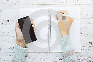 Online education concept with woman hands with pen and modern cell phone on open notebook with clean papers on colored brick