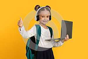 Online Education. Cute Little Schoolgirl With Laptop And Headphones Showing Thumb Up