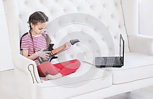 Online education. Girl learns to play guitar at home using laptop.