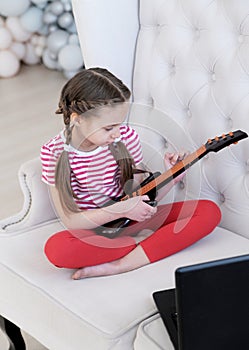 Online education. Girl learns to play guitar at home using laptop.