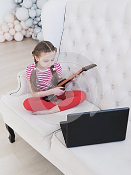 Online education. Girl learns to play guitar at home using laptop.