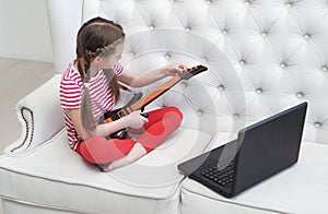 Online education. Girl learns to play guitar at home using laptop.