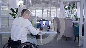 Online education, mature learner crippled in wheel chair writes notes in notebook while watching training sitting at a