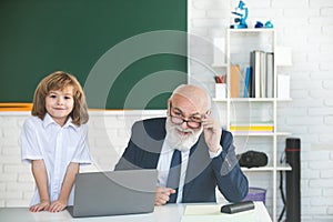 Online education. Old teacher and pupil in school. Schoolboy in classroom with laptop.