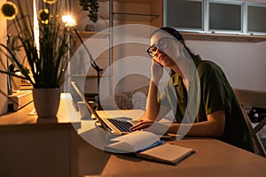 Online education. Portrait of boring young Caucasian woman student working at laptop. Evening in office with electric