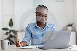 Online Education. Young Black Female Student Using Laptop At Home, Taking Notes