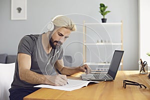 Online education. A young man sitting at a table at home using a laptop and a video call to listen to a lesson online.