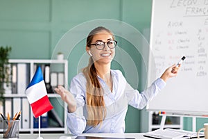 Online foreign languages tutoring. Happy teacher giving French class, pointing at blackboard with basic grammar rules