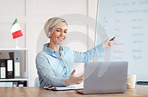 Online foreign languages tutoring. Joyful teacher giving Italian class, pointing at blackboard with basic grammar rules