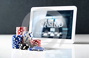 Online gambling on mobile casino concept. Stack of poker chips and tablet with slot machine on screen. Betting on internet.