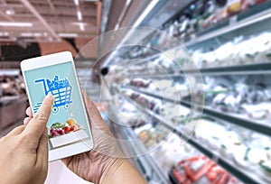 Online grocery shopping concept: Woman hand holding smart phone for ordering food onscreen with icon media on supermarket