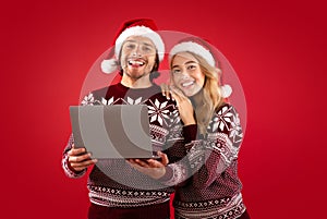 Online holiday shopping. Romantic couple in Christmas outfits with laptop computer on red background