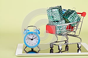 Online, holiday shopping. Supermarket trolley with gift boxes, tablet pc, and clock