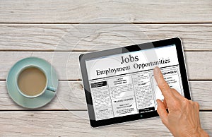 Online job hunting Hand with computer tablet reading employment ads on table with coffee