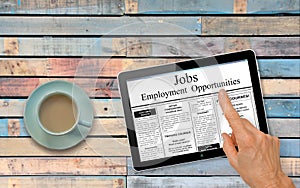 Online job hunting Hand with computer tablet reading employment ads on table with coffee