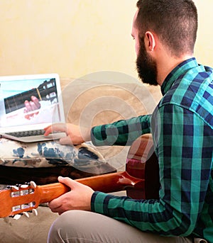 Online learning concept. Young man consulting online guitar course at home