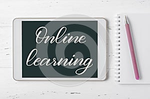 Online learning - handwritten inscription on a tablet. The concept of distance training for children. White wooden background