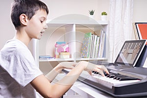 Online learning, remote education. Boy watching video at tablet computer, playing digital piano and singing at home