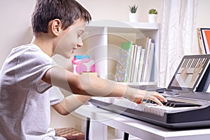 Boy watching video lesson at tablet computer and having fun playing piano at home. Online learning remote education