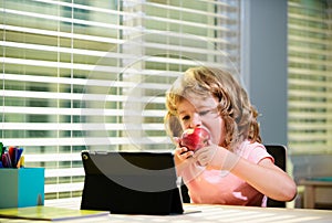 Online lessons for children. Homeschooling and distance kids education. Boy student eat apple, study online with video