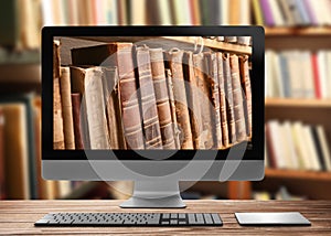Online library. Modern computer on wooden table and shelves with books indoors