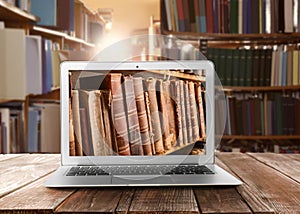 Online library. Modern laptop on wooden table and shelves with books indoors