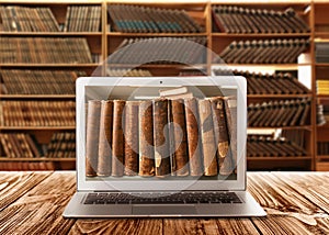 Online library. Modern laptop on wooden table and shelves with books indoors