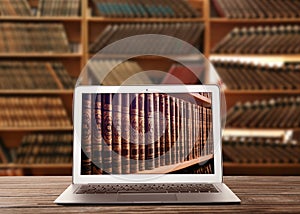 Online library. Modern laptop on wooden table and shelves with books indoors